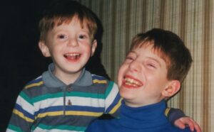 Two boys are smiling while sitting next to each other.