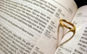 A gold wedding ring sits on top of an open bible.