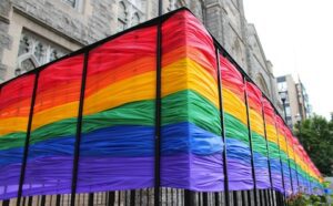A rainbow flag draped over a fence in front of a building.