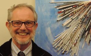 A man smiling in front of a wall of paper.