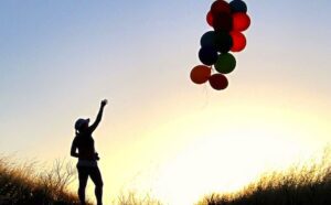 A silhouette of a person holding balloons in the air.