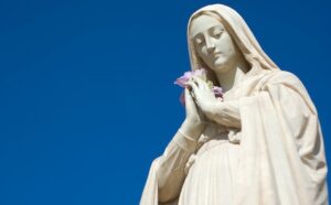 A statue of mary holding a flower against a blue sky.