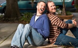 Two men sitting on a bench in front of a house.