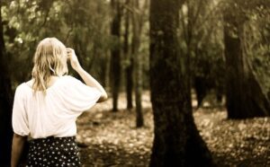 A woman is standing in the woods looking at her phone.