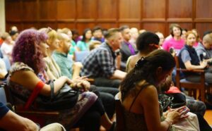 A crowd of people sitting in chairs and listening to a speaker.