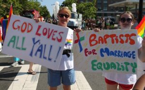 Two women holding signs that say god loves bartists all for marriage equality.