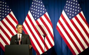 President barack obama speaks at a podium in front of american flags.