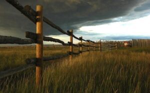 A stormy sky over a fence in a grassy field.
