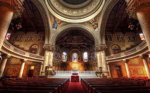 The interior of a church with red pews and an ornate ceiling.