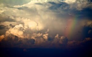 A rainbow is seen above a cloudy sky.
