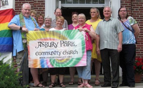 A group of people holding a rainbow flag in front of a house.