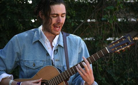 A man with long hair playing an acoustic guitar.