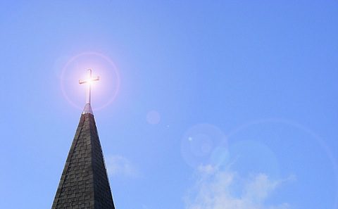 A church steeple with a cross in the sky.