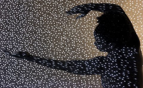 A silhouette of a woman dancing in front of a starry wall.