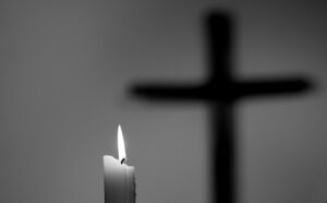 A candle is lit in front of a cross.