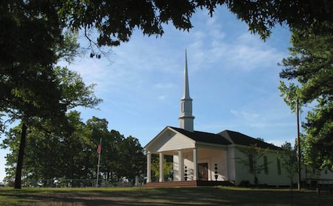 A white church with a steeple surrounded by trees.