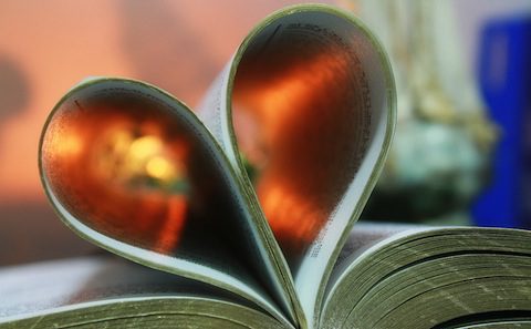 A heart shaped book on a table next to a candle.