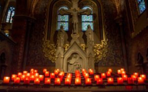 Lit candles in front of a statue in a church.