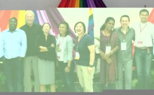 A group of people standing in front of a rainbow flag.