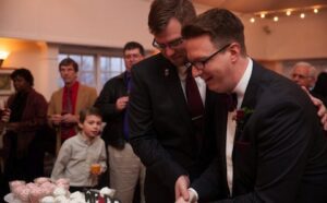 Two men cutting a cake at a wedding.