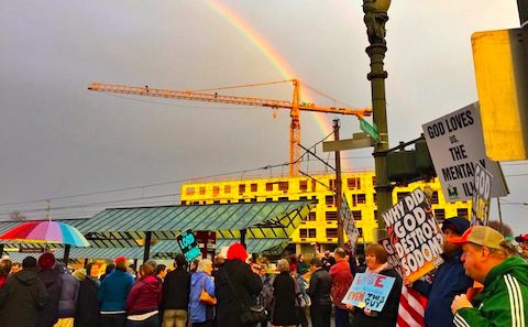 A rainbow over a crowd of people holding signs.