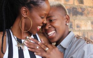 Two black women hugging each other in front of a brick wall.