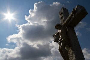 A statue of jesus on a cross in front of a cloudy sky.