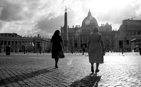 Two women walking down a cobblestone street in front of st peter's cathedral.