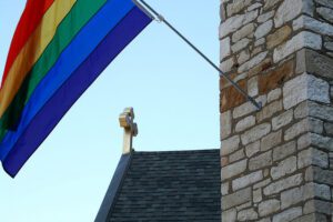 A rainbow flag hangs from the side of a stone building.