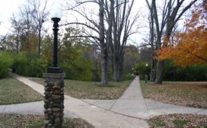 A stone path leading to a park with trees and a lamp post.