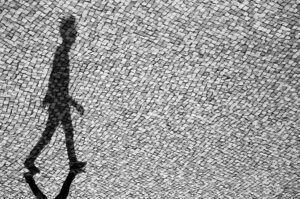 A black and white photo of a person walking on a sidewalk.