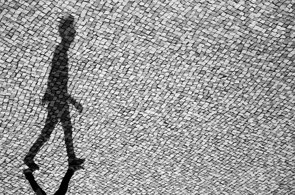 A black and white photo of a person walking on a sidewalk.