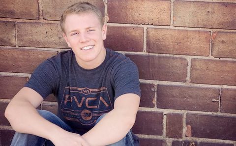 A young man leaning against a brick wall.