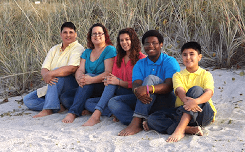 A family sits on the sand in front of tall grasses.