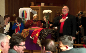 A man in a red tie is singing in a church.