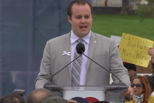 A man in a suit speaking to a crowd of people.