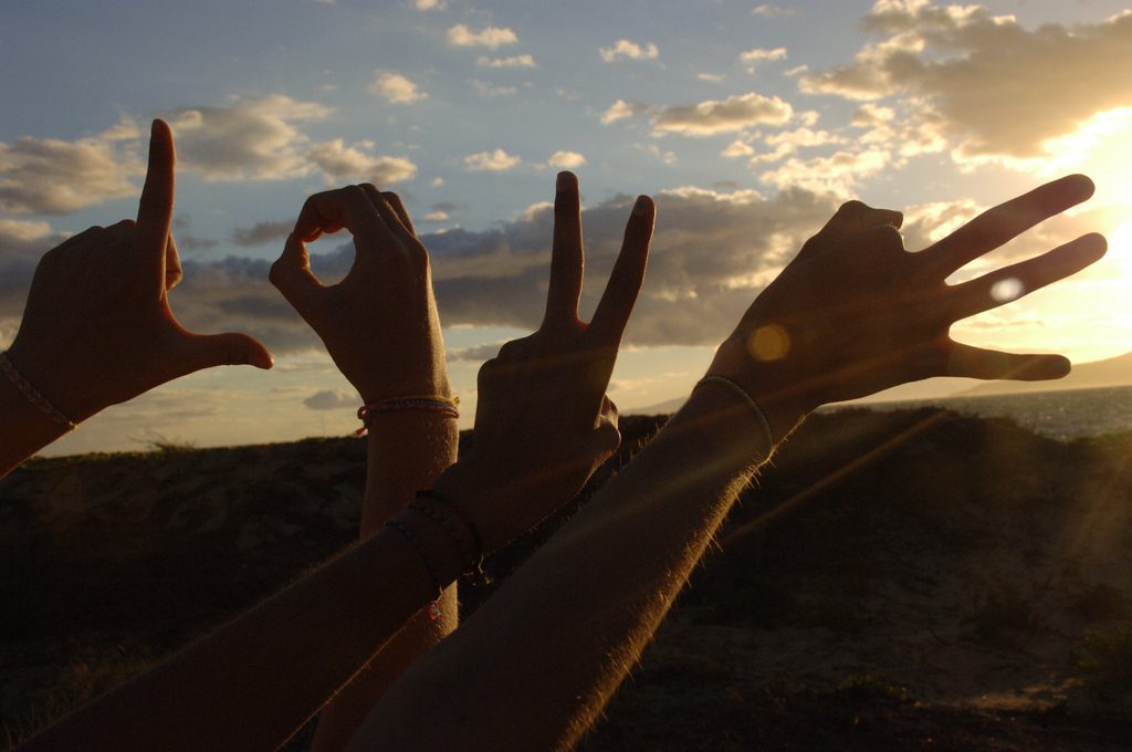 A group of people making a peace sign at sunset.