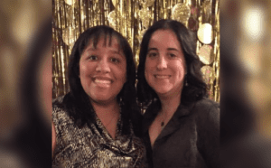 Two women posing for a photo in front of a gold backdrop.