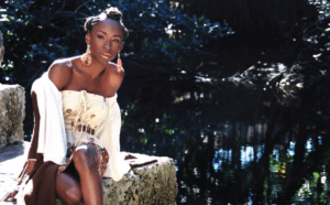 A black woman sitting on a rock next to a pond.