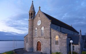 A stone church sits next to a body of water.