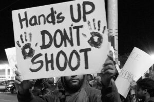 A man holding up a sign that says hands up don't shoot.
