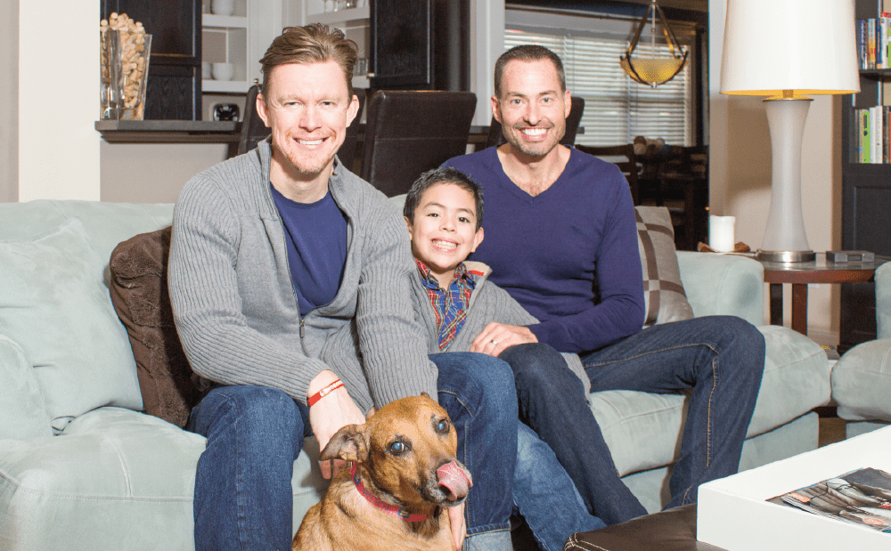 Three men and a dog sitting on a couch in a living room.