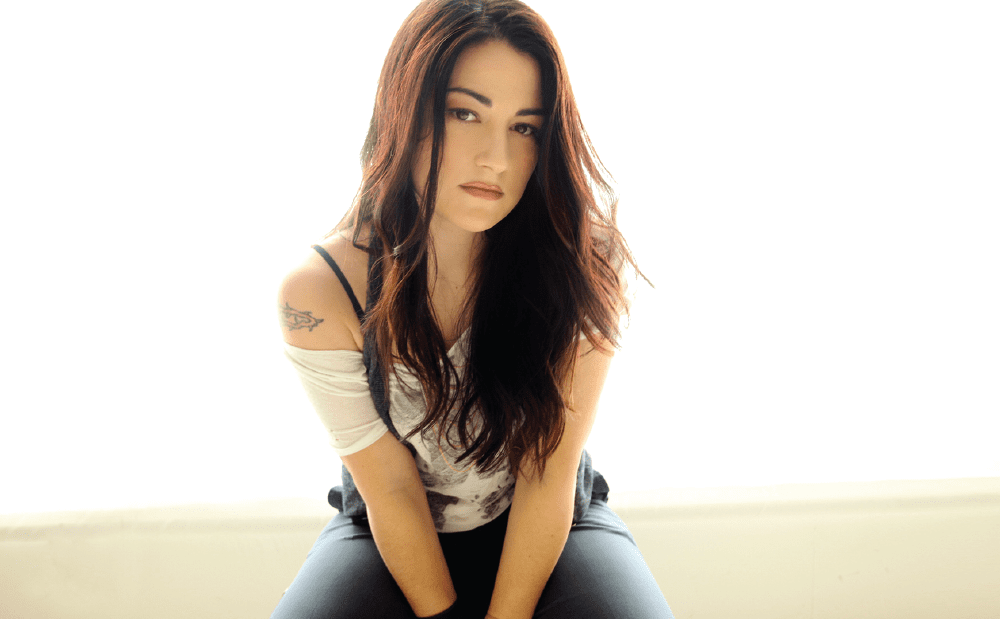 A woman with long hair sitting on a white wall.