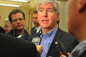 A man in a suit and tie talking to reporters.