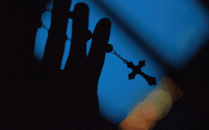 A silhouette of a hand holding a rosary.