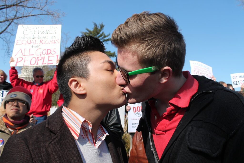 Two men kissing in front of a crowd of people.