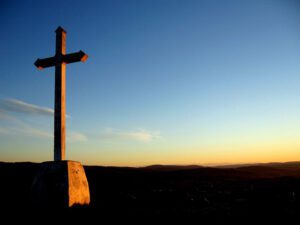 A cross sits on top of a hill at sunset.