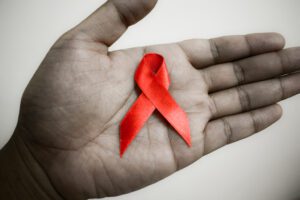 A person's hand holding a red aids ribbon.