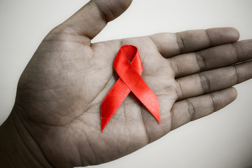 A person's hand holding a red aids ribbon.