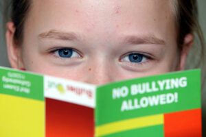 A girl is holding a book that says no bullying allowed.